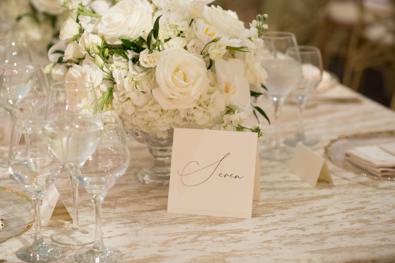 White rose and orchid centerpiece beside a calligraphed table number