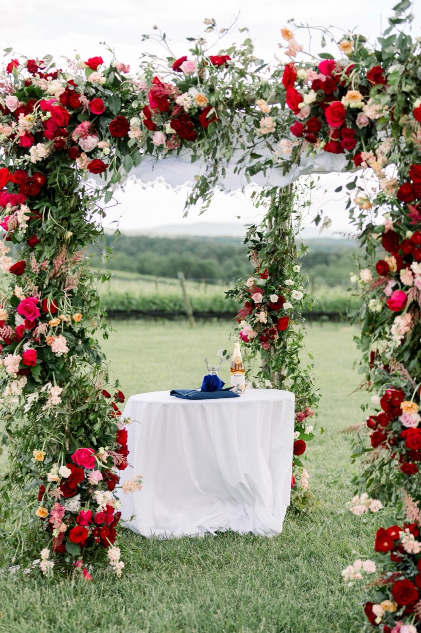 Four-post chuppah in garden roses overlooking a vineyard, designed by the studio that runs on Florio