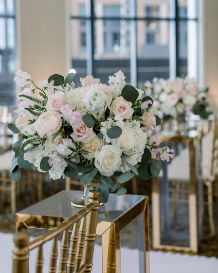 Blush ranunculus and rose compote in a gold vessel beside gold chiavari chairs