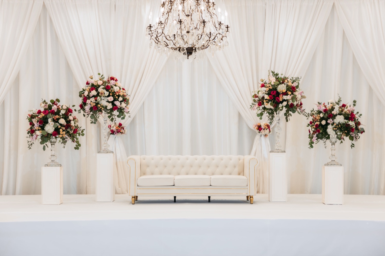 Cream tufted chesterfield sofa staged under a chandelier with floral pedestals