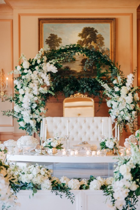 Greenery moon gate framing a tufted sweetheart table in a paneled salon